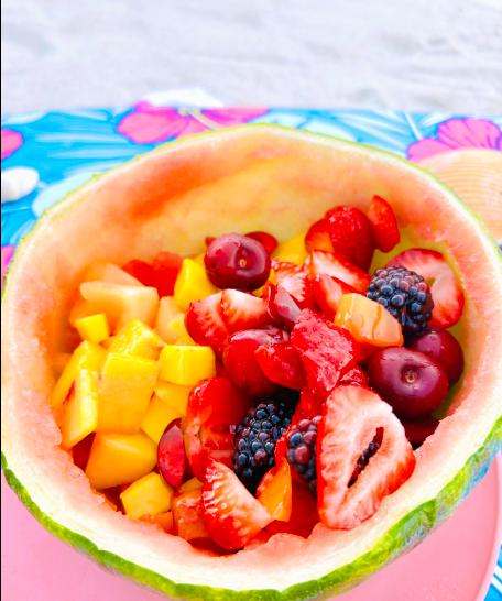 Friss gyümölcsök, köztük eper, szeder, mangó és cseresznye, egy félbevágott görögdinnyehéjban.